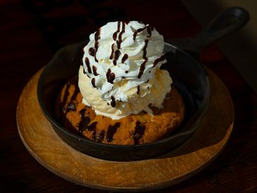 Skillet cookie topped with vanilla ice cream, whipped cream, and chocolate drizzle.