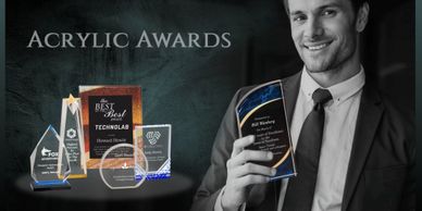 Man holding an acrylic award with more awards displayed.