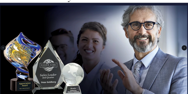 Smiling businessman applauding next to sales awards and trophies.