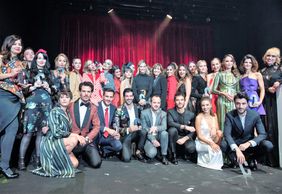 About 30 people on stage with red curtains in the background. Everyone is formally dressed in gowns