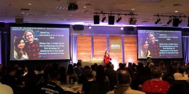 Dona standing on the Microsoft Ability stage in a red silk dress with screens on both sides of her