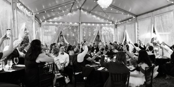 Guests raise glasses in a celebratory toast under a lit tent.