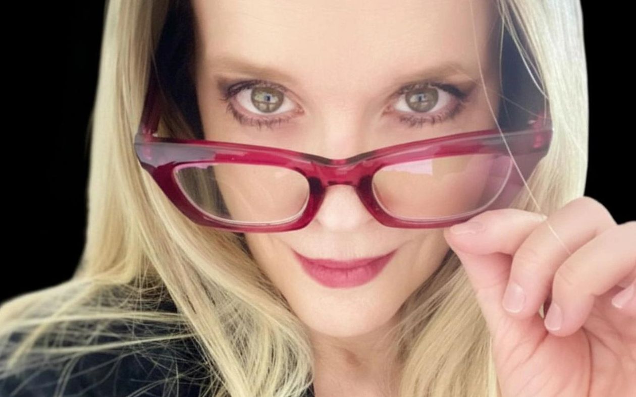 Serious and mischievous looking blond woman looking over her glasses