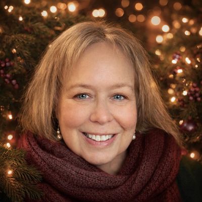 Smiling woman wearing a burgundy scarf in front of festive holiday lights.