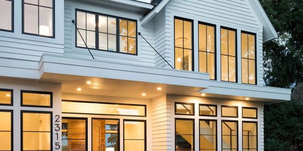 Modern two-story house with large windows and warm lighting.