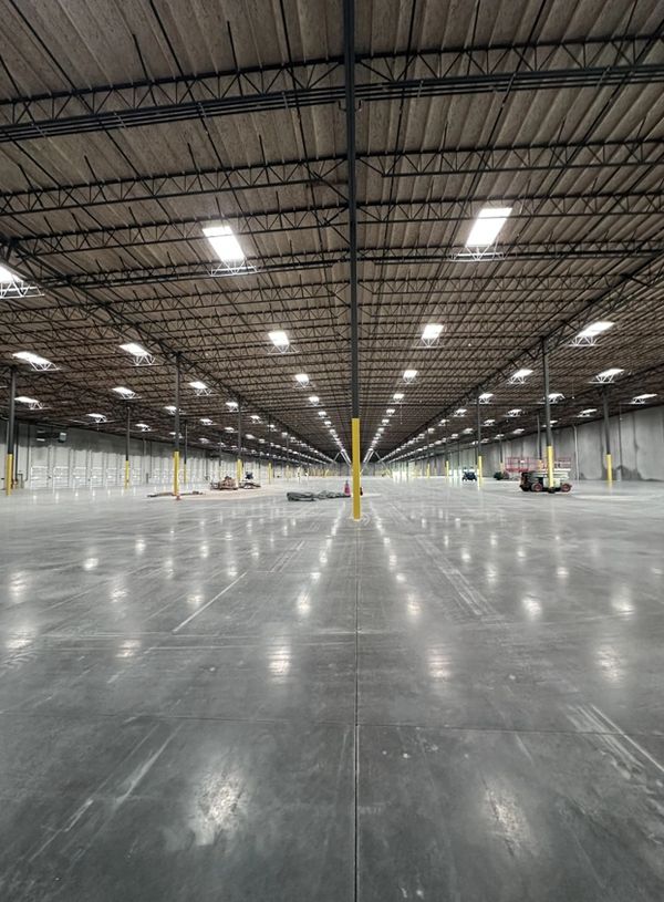 Vast empty warehouse with polished concrete floors and ceiling lights.