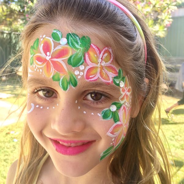 Smiling girl with colorful floral face paint and pink lipstick outdoors.