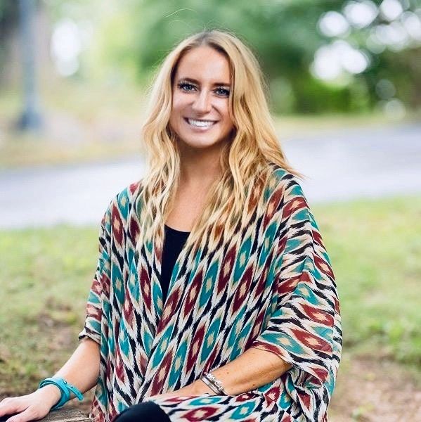 Smiling woman with long blonde hair wearing a colorful patterned shawl outdoors.