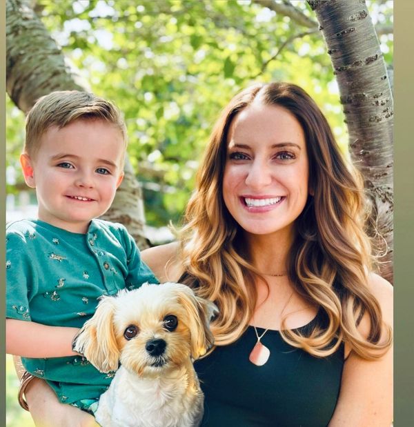 Smiling woman and child holding a small dog outdoors.