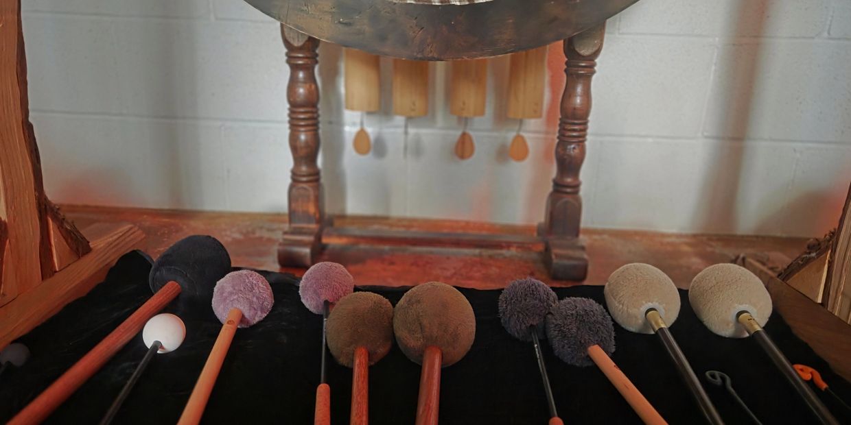 Various mallets arranged in front of a large gong with a wooden stand.