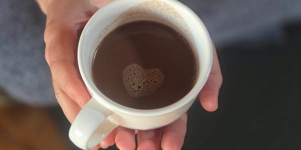 A cup of hot chocolate with a heart-shaped foam held in hands.