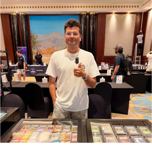 A man in a white t-shirt giving a thumbs up at a trading card event.