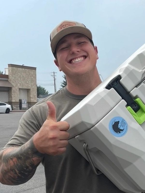 Man smiling and giving thumbs up holding a cooler.