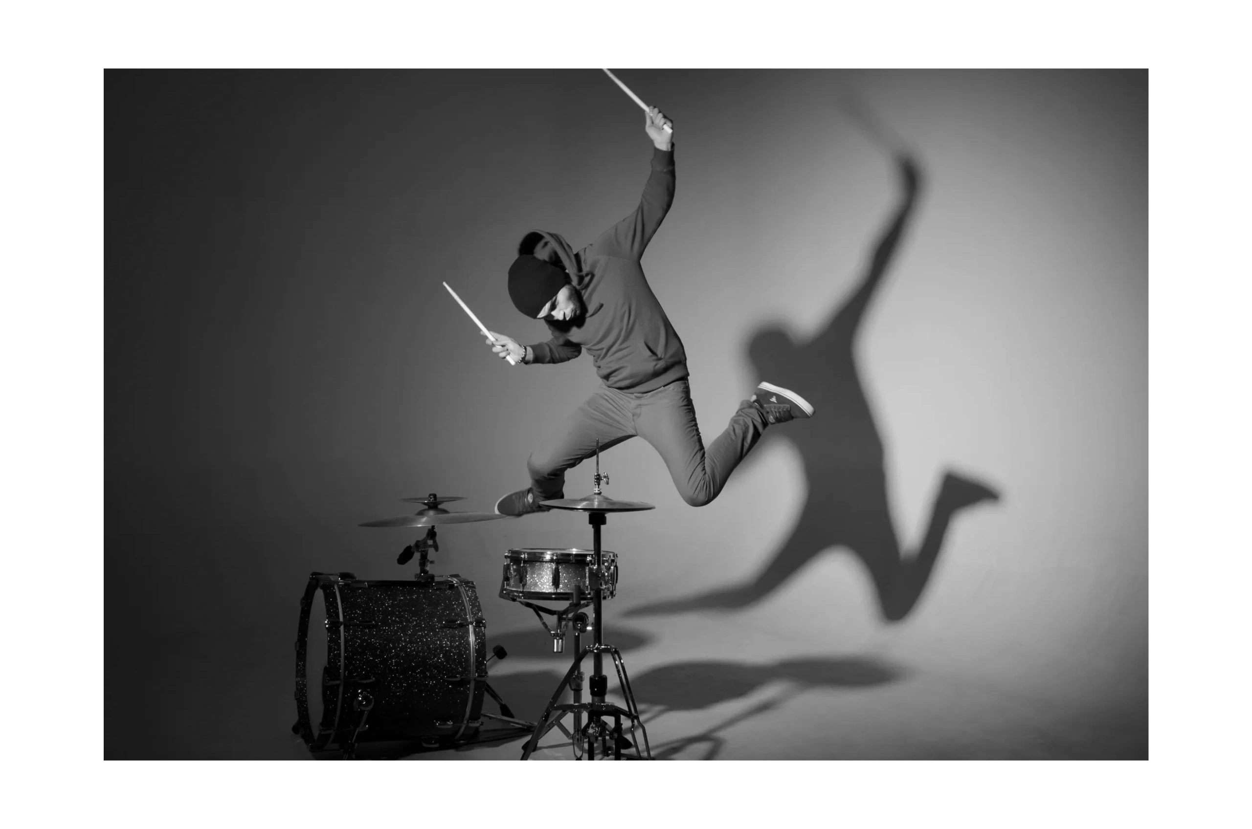 Drummer in a red hoodie jumping high while holding drumsticks.