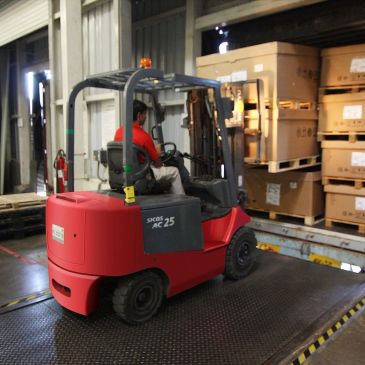 A red forklift moving near stacked boxes in a warehouse.