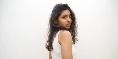 A woman with long hair looks over her shoulder against a plain white background.