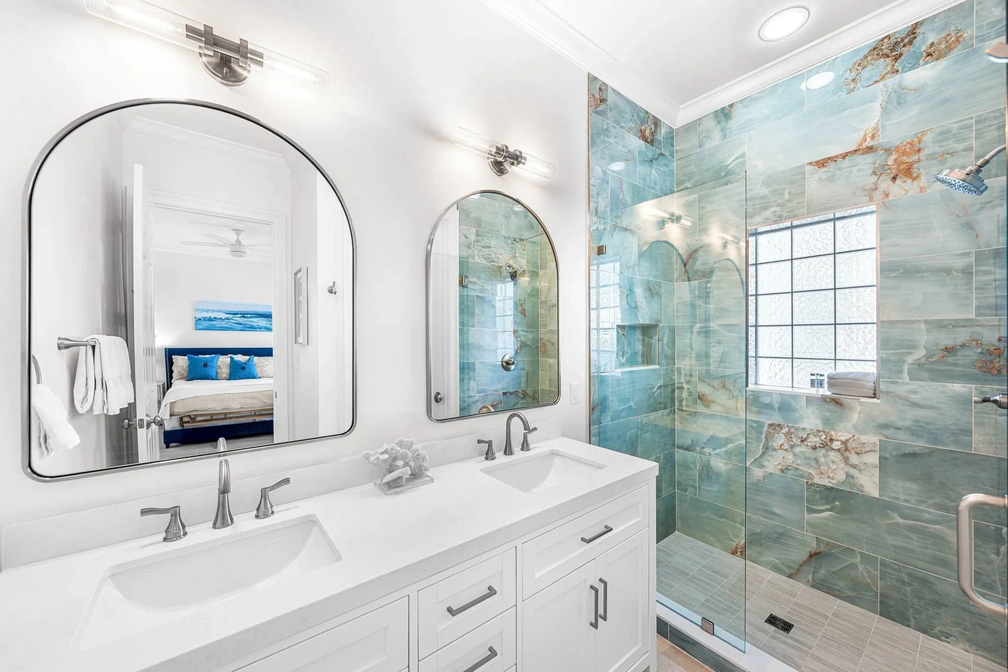 Modern bathroom with dual sinks and blue-green tiled shower.