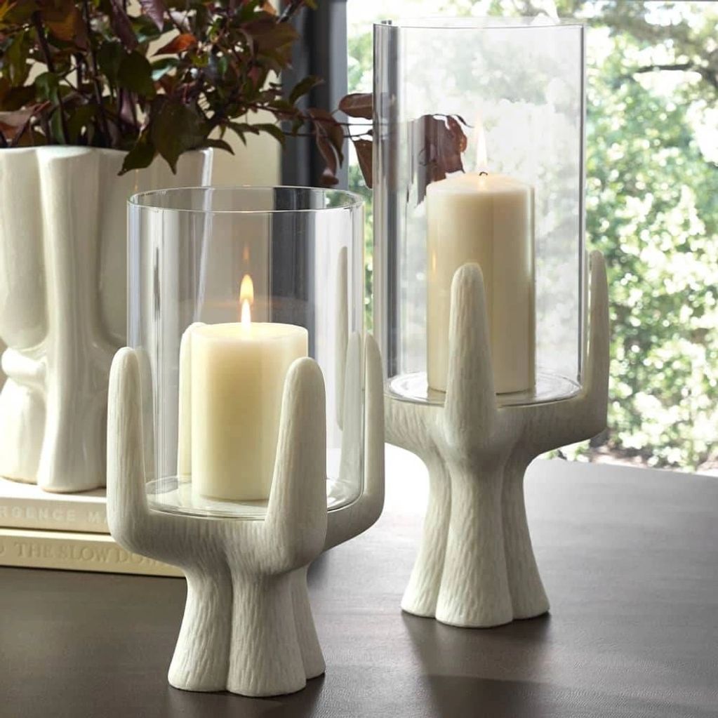 Two modern candle holders shaped like cacti with lit candles inside.