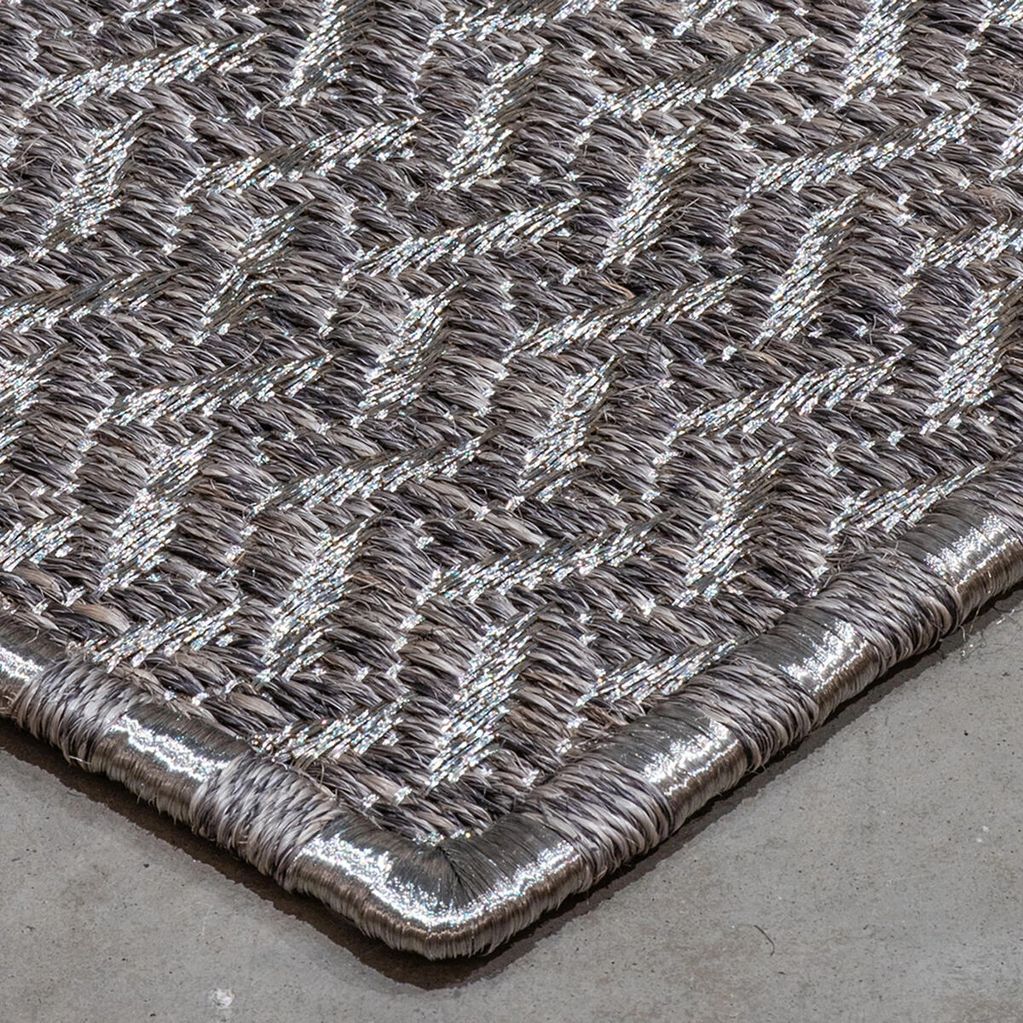 Close-up of a woven rug with metallic silver accents on a concrete floor.