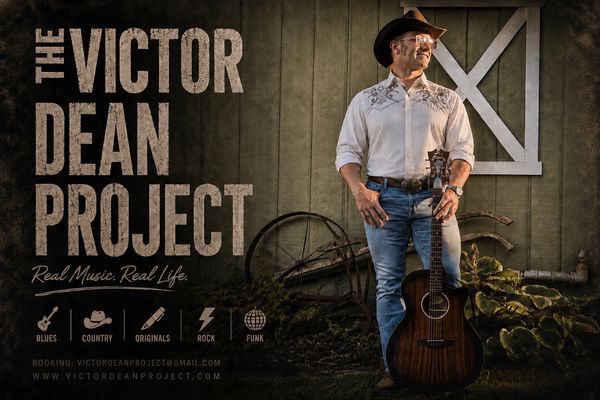 Man with guitar in front of rustic wall for The Victor Dean Project.