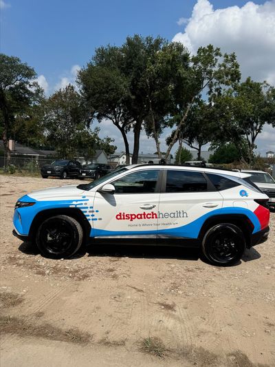 A white and blue DispatchHealth SUV parked outdoors on a dirt surface.