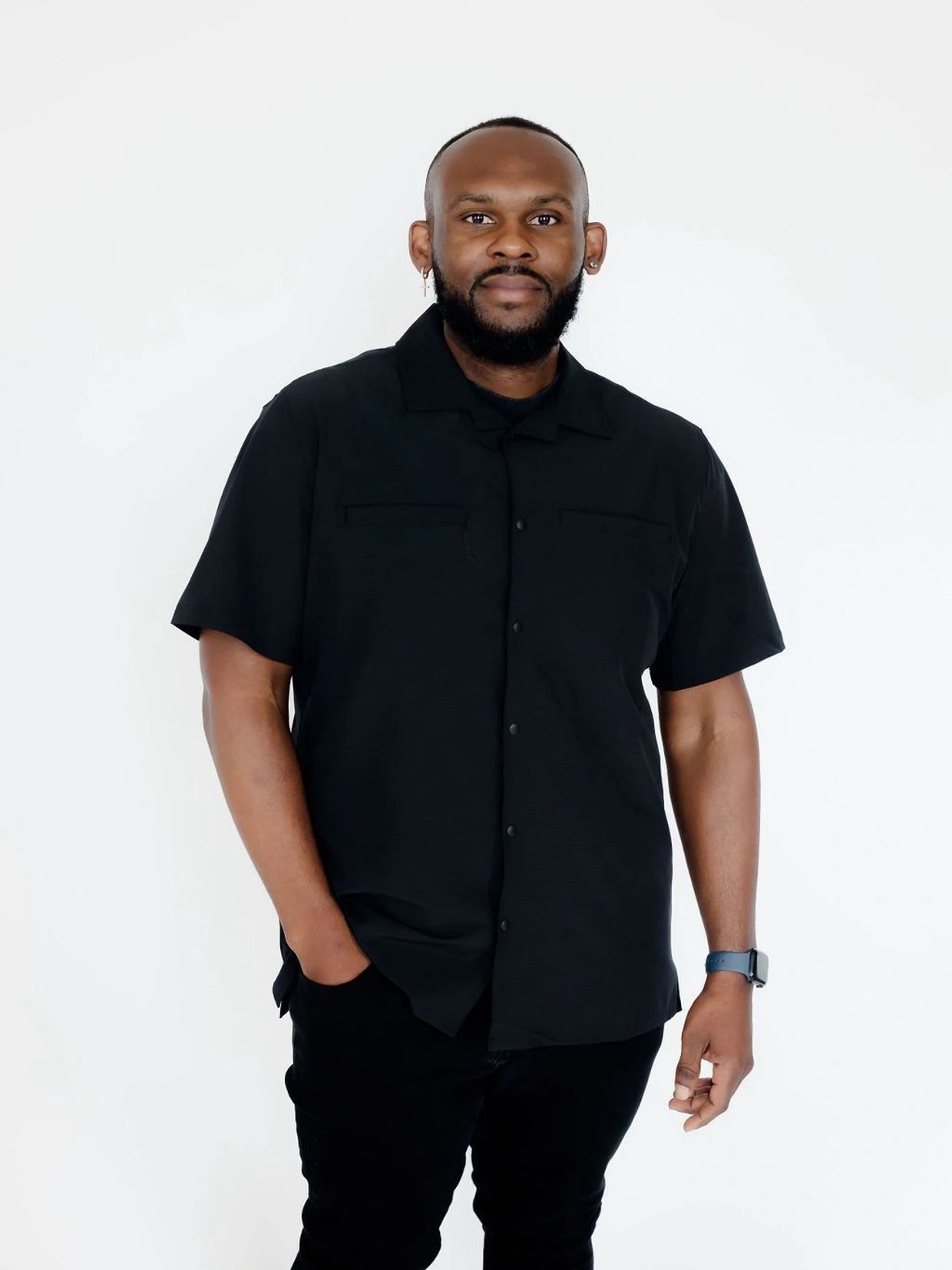 Man in black shirt and pants standing against white background.