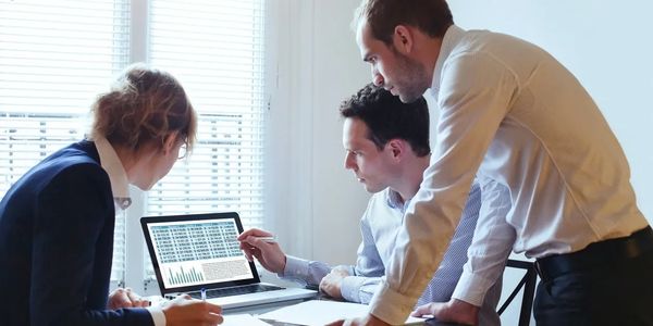Three professionals analyzing data on a laptop in a meeting.