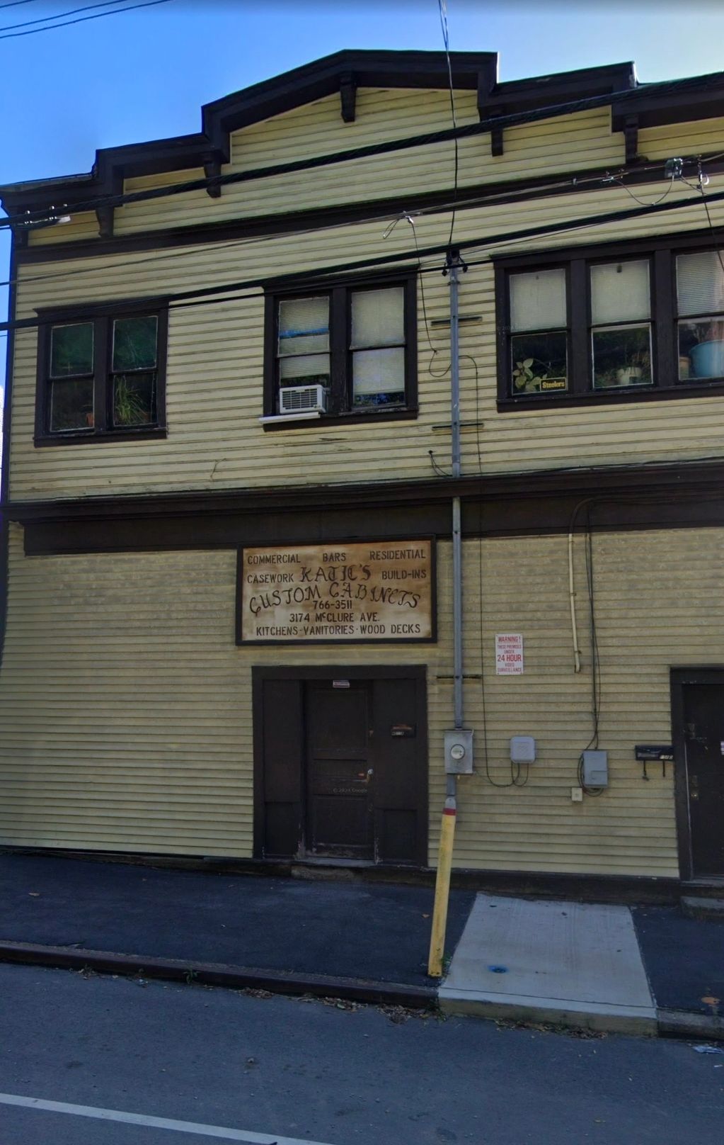 Old yellow building with a sign for Kajic's Custom Cabinets and dark doors.