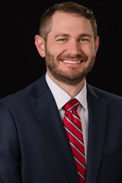 Professional man in suit with red striped tie smiling against black background.