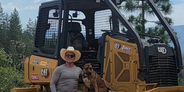 Man in cowboy hat with dog on construction vehicle.