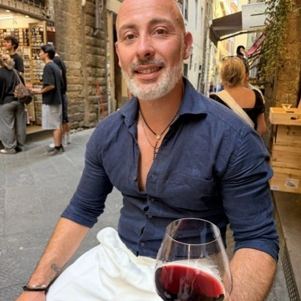 Man enjoying red wine outdoors in a lively street.