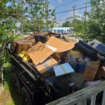 A trailer filled with discarded furniture and boxes on a sunny day.