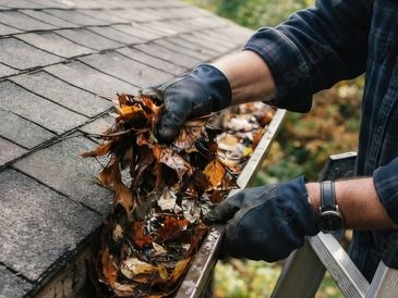 Person cleaning leaves from gutter wearing gloves.