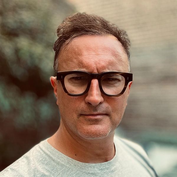 Man with glasses posing outdoors with a neutral expression.