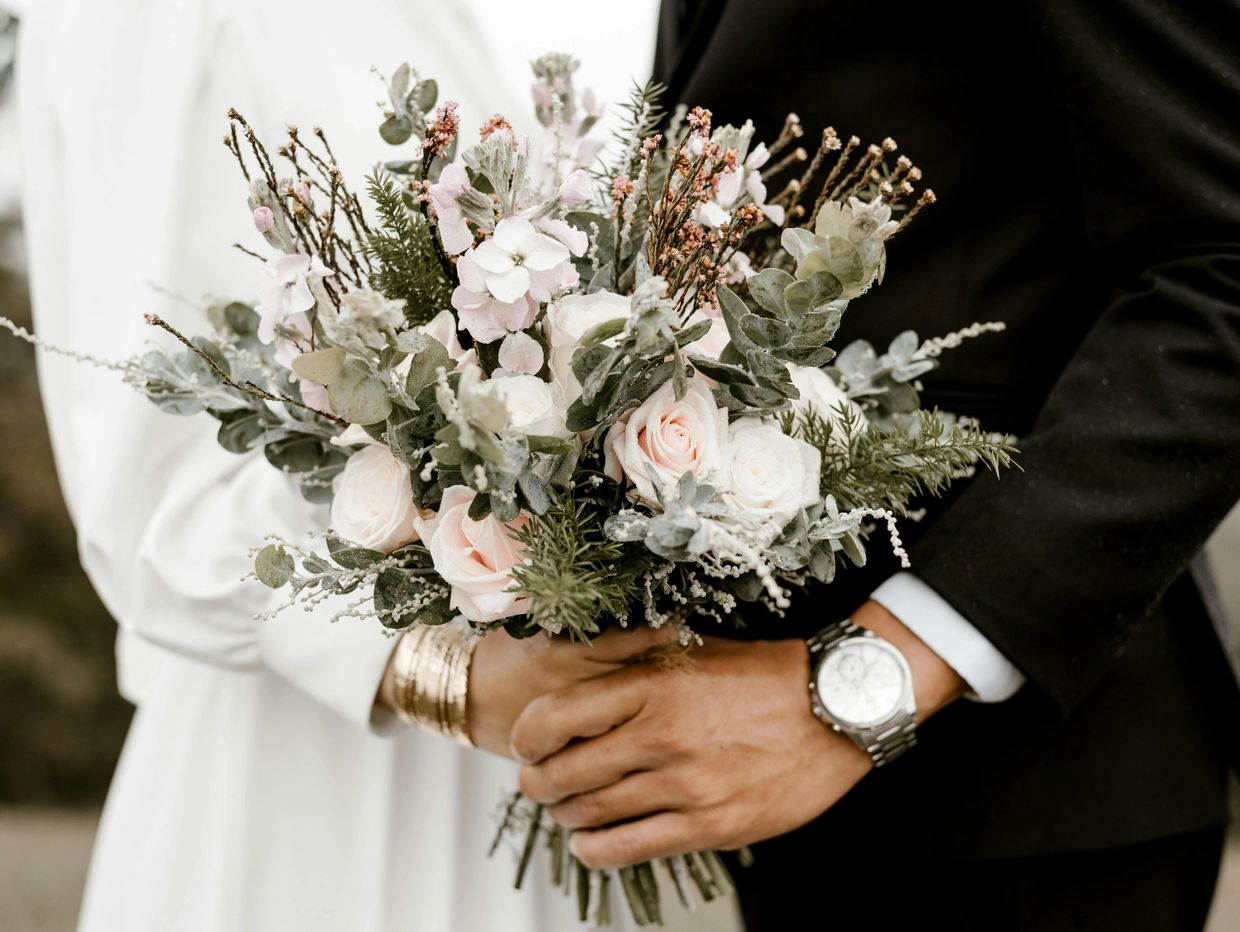 Couple holding a delicate bouquet of flowers together, symbolizing unity.
