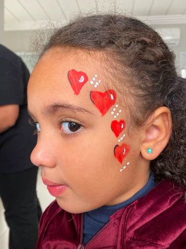 Child with red heart face paint on cheek looking to the side.