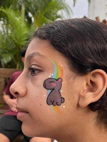Side profile of a girl with colorful face paint of a cartoon dog and rainbow.