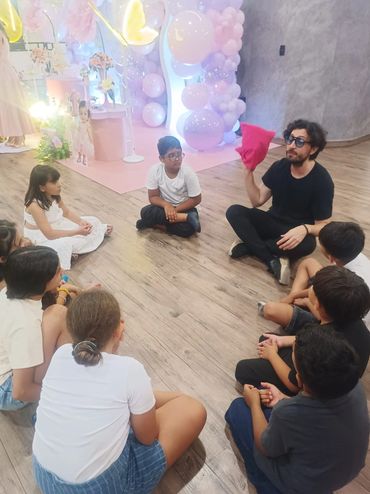 Adult reading or performing for children seated in a circle on the floor.