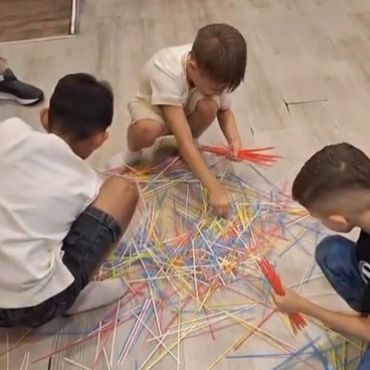 Three boys playing a game with colorful sticks on the floor.