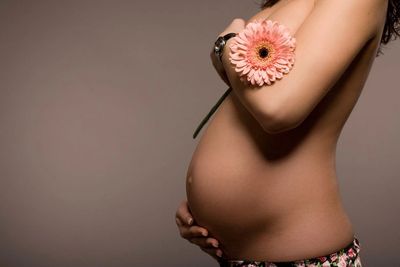 Person caressing pregnant stomach whilst holding flower