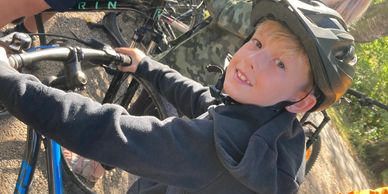 A young boy wearing a helmet is on a bicycle, smiling at the camera.