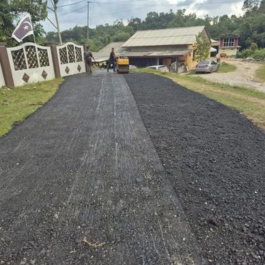 Road being paved with asphalt near houses in a rural area.