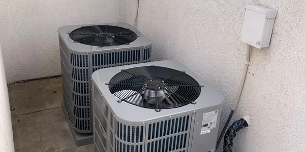 Two outdoor air conditioning units installed against a white wall.