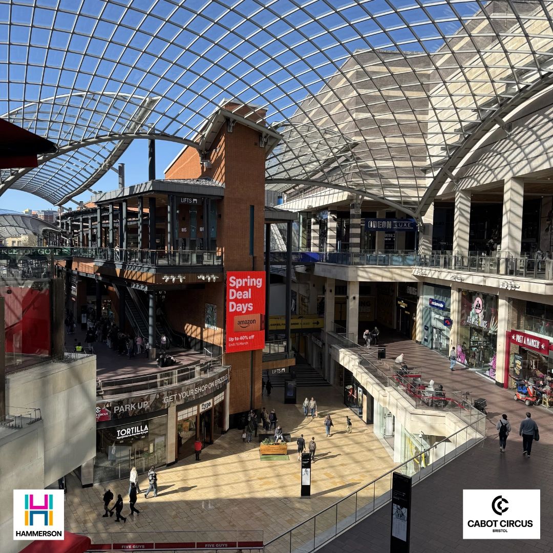 Modern shopping center with glass ceiling and various shops.