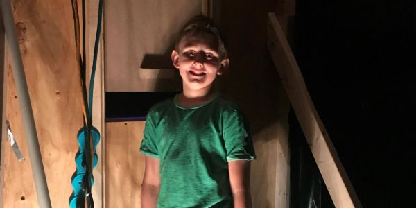 Boy standing in a wooden room with shadowy lighting.
