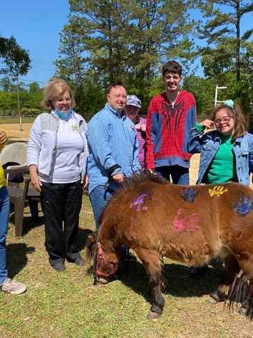 Group of people smiling outdoors with a small painted pony.