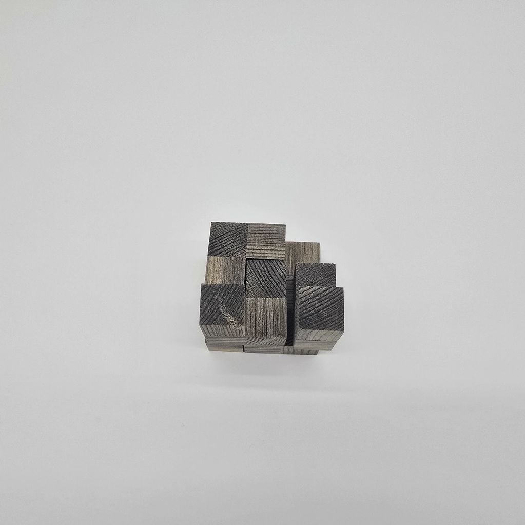 A wooden puzzle cube made of small dark wooden blocks on a white surface.