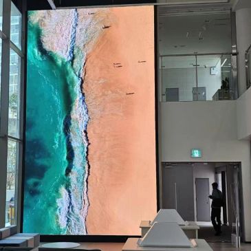 Large vertical screen displaying an aerial beach view inside a modern building.
