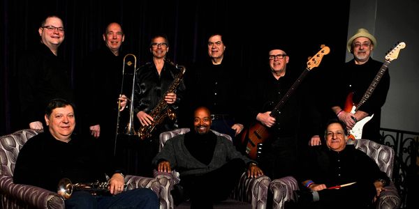 A diverse band of nine male musicians posing with instruments.