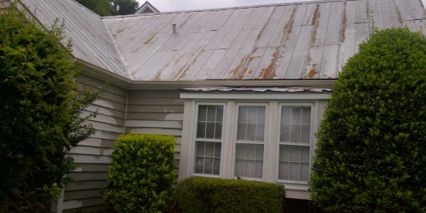 Old house with rusty metal roof and bushes.